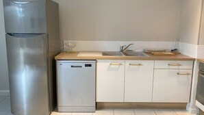 Eine Küche mit einem Edelstahlkühlschrank, einem Geschirrspüler, einer Spüle mit Wasserhahn und Holzschränken.