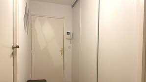 Ein schmaler Flur mit einer weißen Tür, einer kleinen schwarzen Bank und einem Thermostat an der Wand.