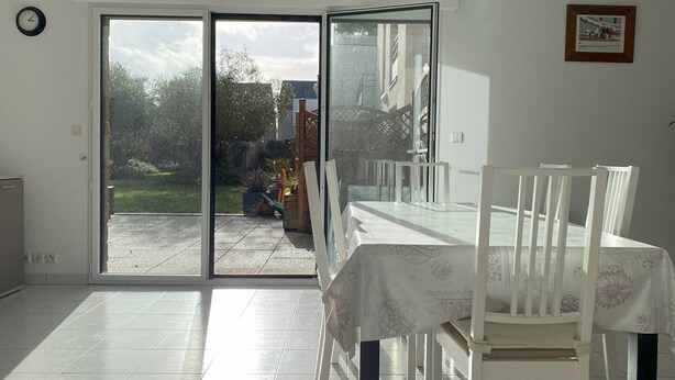 Ein Zimmer mit einer Schiebetür zum Garten, einem Esstisch mit Stühlen und einer Wanduhr.