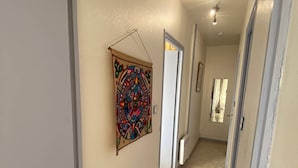 A hallway with a colorful tapestry on the wall, a door leading to another room, and a light fixture on the ceiling. - Duplex T3 Sea View, Sleeps 6, Terrace, Parking, Barcarès (Le Barcarès)