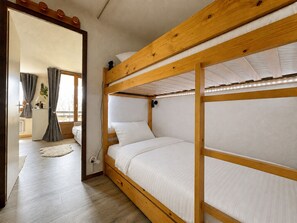 Ein Schlafraum mit Etagenbetten, Holzrahmen, weißer Bettwäsche und einer sichtbaren Steckdose an der Wand.