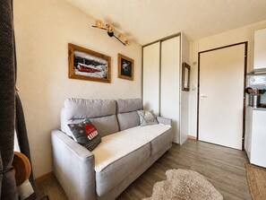 A neutral-toned living room with a grey sofa, a white door, and two framed pictures on the wall. - Modern and bright studio with views of Mont Charvin. Private parking (Notre-Dame-de-Bellecombe)