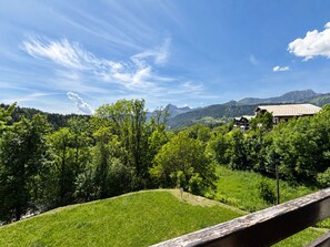 Un paysage montagneux avec une maison entourée d’une végétation luxuriante et un ciel dégagé.
