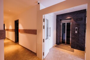 A modern hallway with a marble wall, an elevator, and a door with a handle.