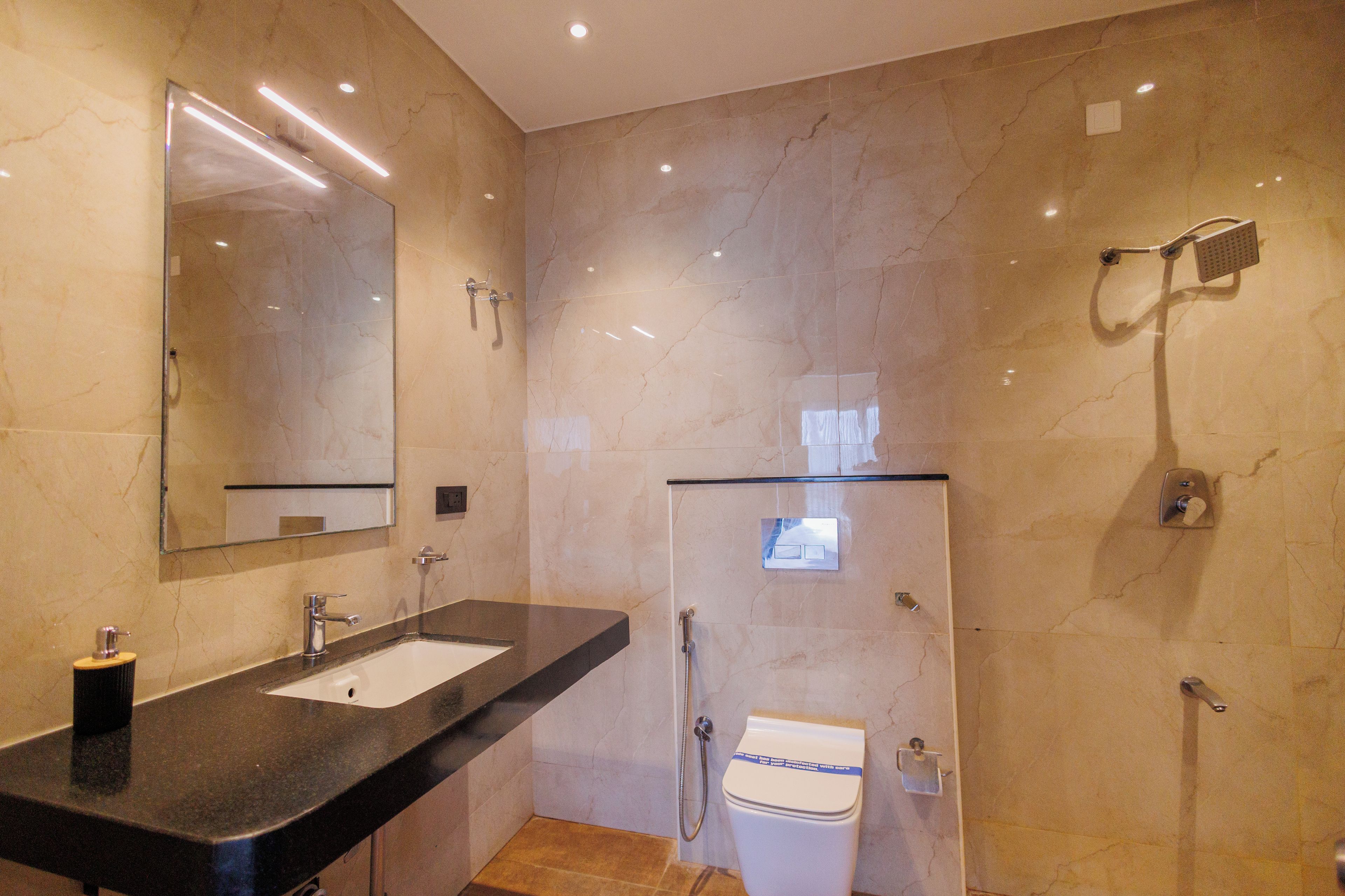 A modern bathroom with a marble floor, a black countertop sink, a mirror, a shower, and a toilet.