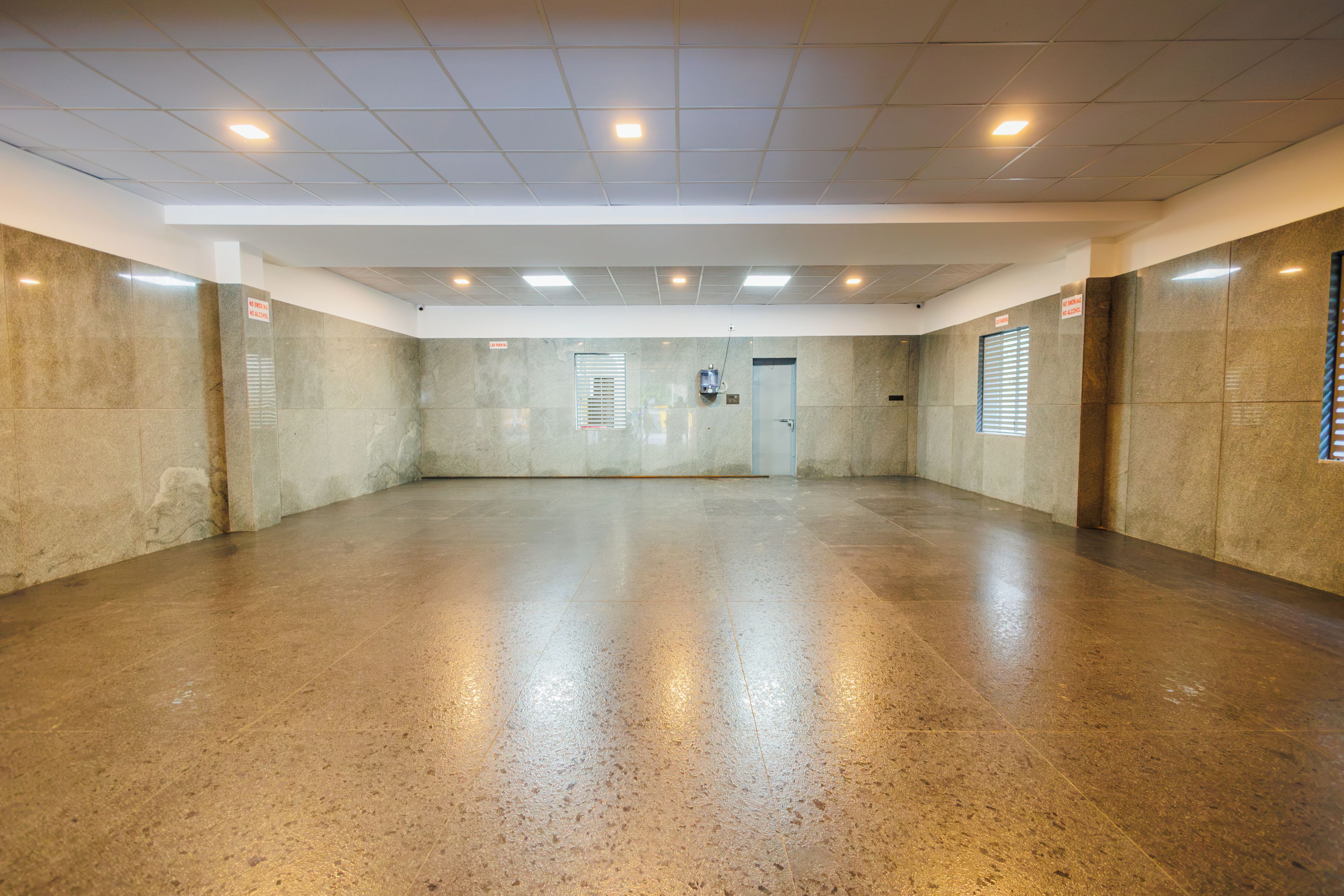 A spacious, empty room with a polished floor, a door, and a window with blinds.