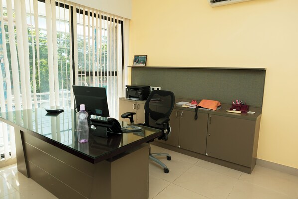A modern office with a glass desk, black office chair, and a printer on a shelf. - Mas Residency (Tiruvannamalai)