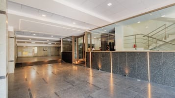 A modern lobby with a reception desk, glass doors, and a staircase.