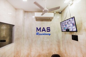 A ceiling fan, an air conditioning unit, a security camera, and a television mounted on a wall with a sign reading 'MAS Residency'.