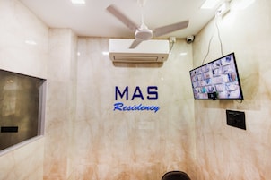 Un ventilador de techo, un equipo de aire acondicionado, una cámara de seguridad y un televisor montado en la pared con un letrero que dice 'MAS Residency'.
