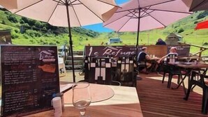 Een terras met houten tafels en stoelen, parasols en een menubord.