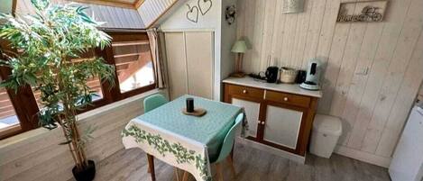 A compact room with a dining table, a small kitchen area, a potted plant, and a skylight.