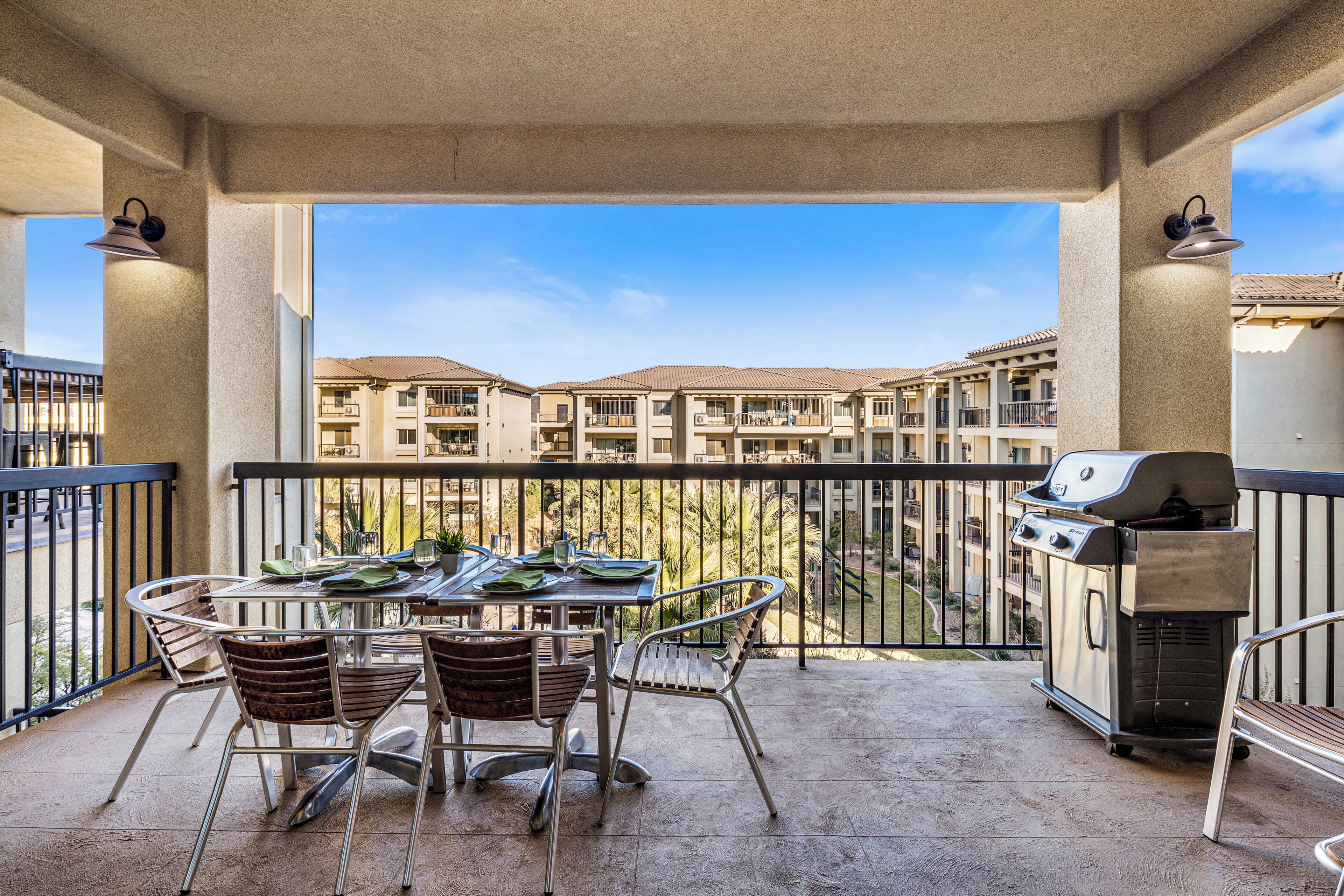 Een balkon met een tafel, stoelen, een barbecue en uitzicht op appartementencomplexen.