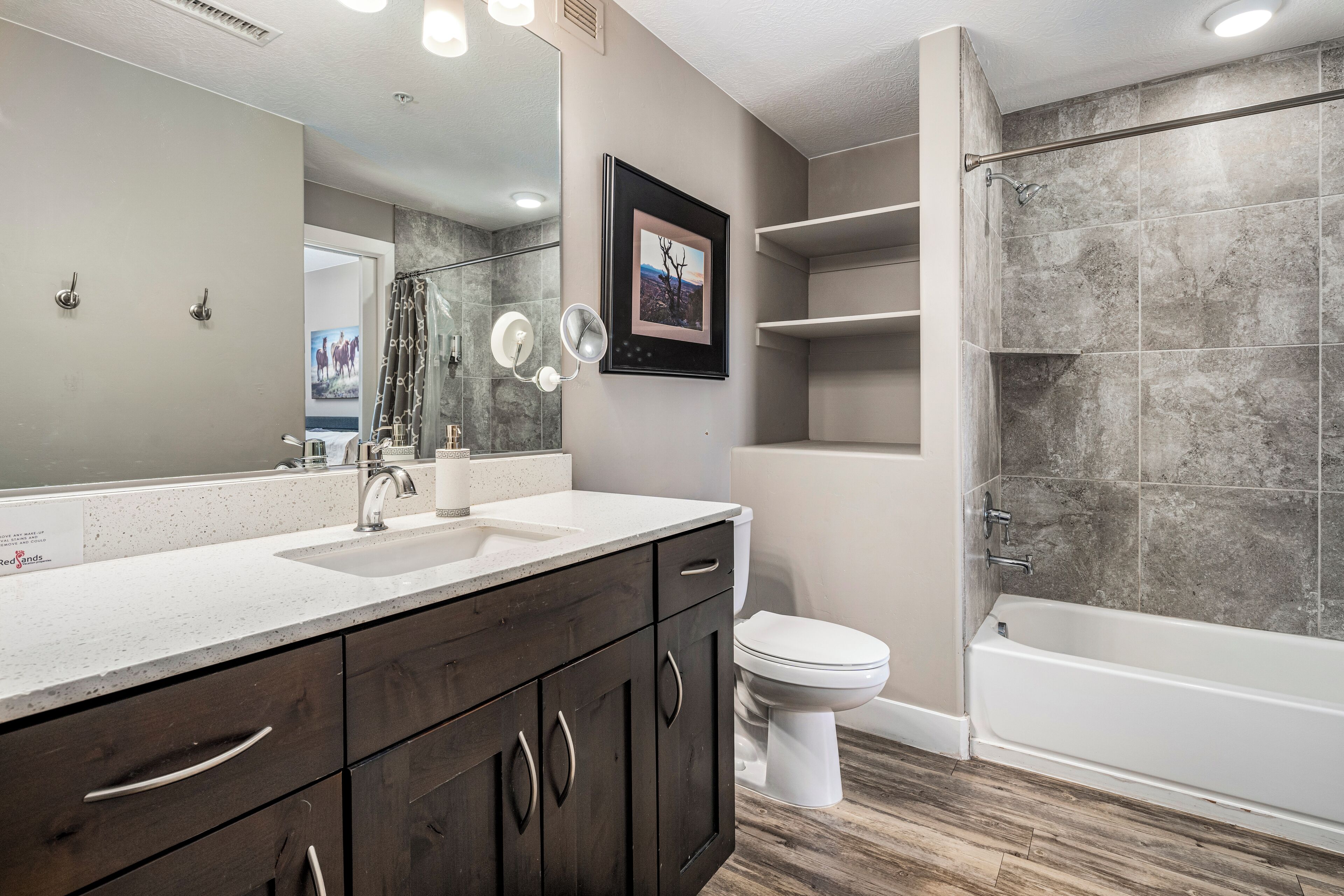 Un baño moderno con un espejo grande, armarios de madera oscura, un lavabo blanco y una zona de ducha.