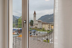 Une vue depuis un balcon orné d’une balustrade en métal, avec une tour de pierre et un paysage montagneux en arrière-plan.