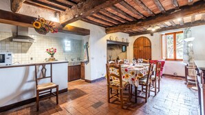 A rustic kitchen with wooden beams, a dining area with a table set for four, and a large arched doorway. - Apartment 'Green  Siena' with Shared Pool, Private Terrace and Wi-Fi (Siena)