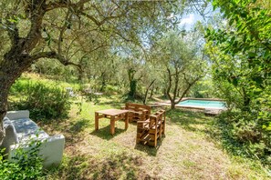 A garden with a wooden table and chairs, a stone bench, and a swimming pool. - Apartment 'Green  Siena' with Shared Pool, Private Terrace and Wi-Fi (Siena)