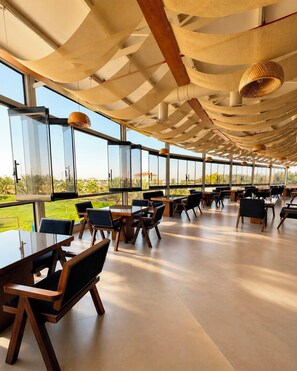 A spacious indoor area with tables and chairs, large windows offering a view of the outdoors, and a ceiling with a unique woven design. - vista hotel (Tabuk)