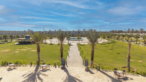 A pathway leading to a pool area with palm trees and outdoor seating. - vista hotel (Tabuk)