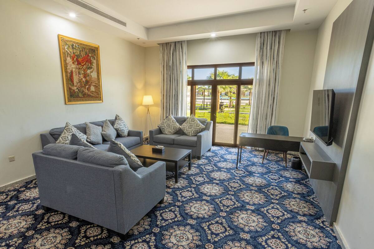 A modern living room with a blue patterned carpet, grey sofas, a coffee table, and a television.