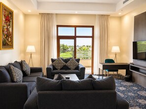 A hotel room with a sofa set, a desk, a television, and a view of a landscaped area. - vista hotel (Tabuk)