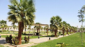 A well-maintained outdoor area with palm trees, a covered seating area, and a pathway. - vista hotel (Tabuk)