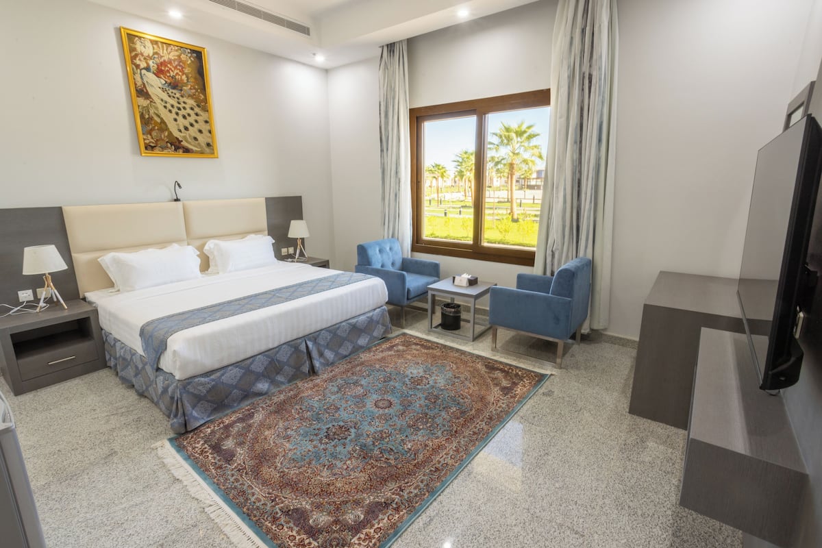 A hotel room with a large bed, a blue armchair, a small table, and a TV.