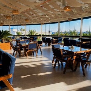 A modern dining area with tables and chairs, large windows, and a view of palm trees. - vista hotel (Tabuk)