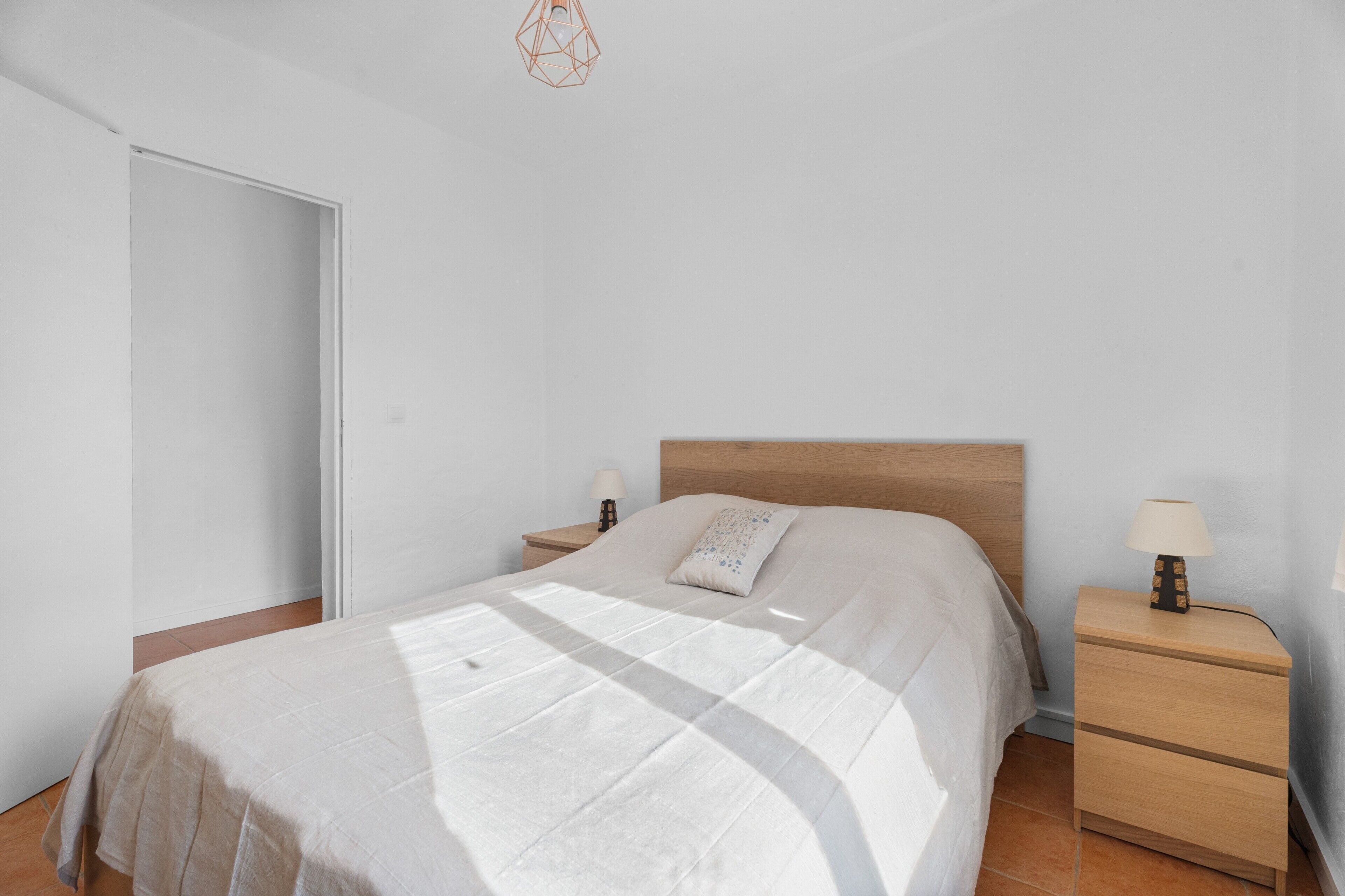 Une chambre à coucher comprenant un lit, deux tables de chevet, une commode, une porte et un luminaire suspendu.