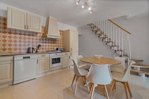 A modern kitchen with white cabinets, a dining area with a wooden table and white chairs, and a staircase with wooden steps and metal railings. - Domaine de Oliviers – Provençal house with garden and pool in Hyères, 10 min from beaches (Hyères)