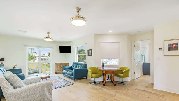 A spacious living room with a sofa, a dining table with chairs, and a TV mounted on the wall.