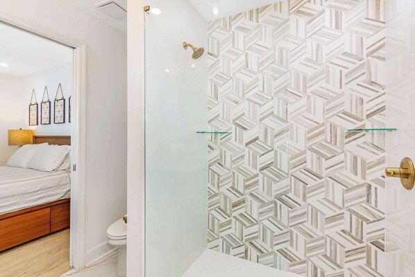 Un baño moderno con pared de diseño geométrico, cabina de ducha de vidrio y un inodoro a la vista.