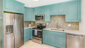 A modern kitchen with teal cabinets, stainless steel appliances, and a patterned backsplash.