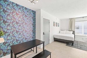 Un dormitorio con cama, escritorio, banca, pared con diseño y ventana con cortinas.