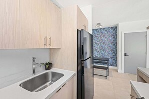 Una cocina moderna con armarios de madera clara, un lavamanos de acero inoxidable y un refrigerador negro.