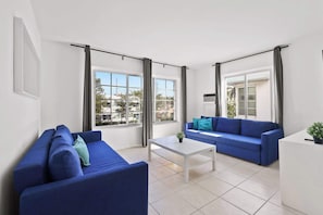 Un salón moderno con un sofá azul, una mesa de centro blanca y vistas al exterior.