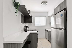 Una cocina moderna con un refrigerador de acero inoxidable, estufa integrada y una ventana con persianas.