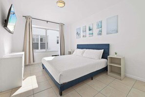 A bedroom with a bed, a TV mounted on the wall, a window with curtains, and artwork on the wall.