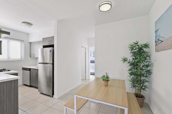 A modern kitchen with stainless steel appliances, a wooden dining table, and a potted plant.