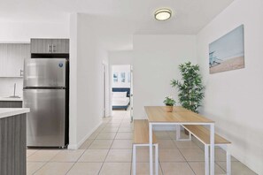 A modern kitchen with a stainless steel refrigerator, a wooden dining table, and a potted plant.