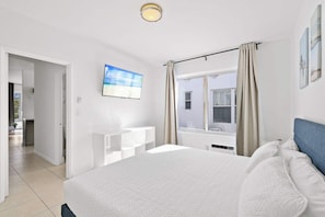Habitación de hotel con cama, televisor montado en la pared, ventana con cortinas y vista al exterior.