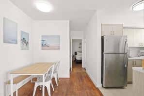 A modern kitchen with a stainless steel refrigerator, white cabinetry, and a wooden dining table with chairs.