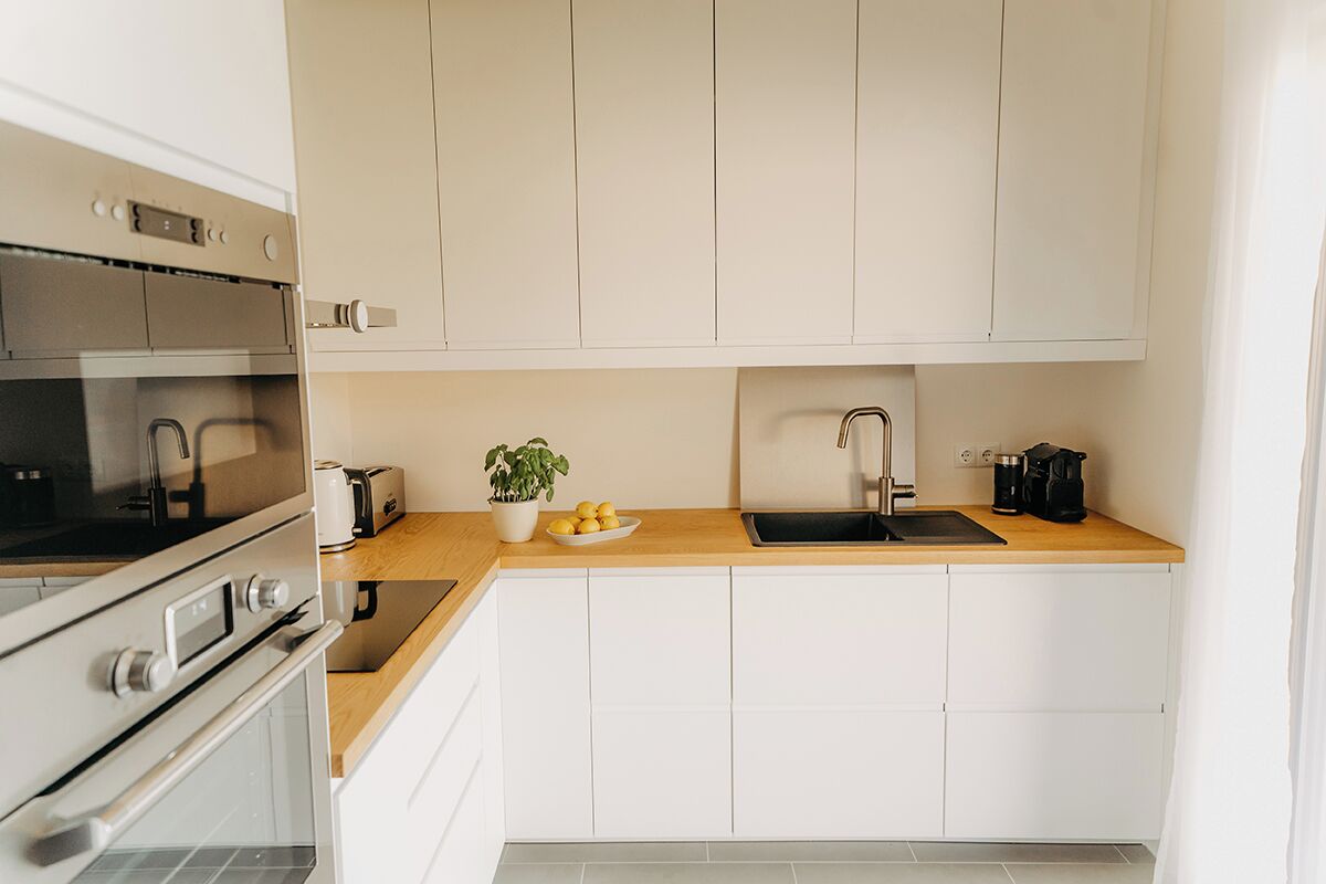 A modern kitchen with white cabinets, a stainless steel oven, a sink, and a wooden countertop.