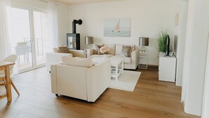 Een moderne woonkamer met een witte bank, een salontafel en een open haard. Er is een schuifdeur van glas die leidt naar een buitenruimte.