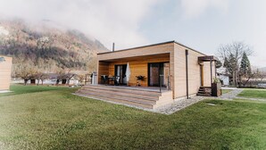 Een modern huis met een houten gevel, een overdekte patio en uitzicht op een bergachtig landschap.