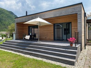 A modern wooden house with a covered patio, outdoor seating, and a view of a mountainous landscape. - Drauinsel Chalet Linsendorf (Gallizien)