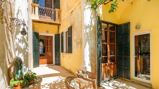 A courtyard with wicker chairs, a potted plant, and a balcony with a railing. - Charming Villa 'Cas Sitger' in the Heart of Felanitx – Garden, Terraces & Wi-Fi (Felanitx)