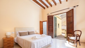 A bedroom with a bed, bedside table, chair, and a door leading to an outdoor area. - Charming Villa 'Cas Sitger' in the Heart of Felanitx – Garden, Terraces & Wi-Fi (Felanitx)