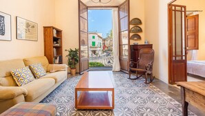 A cozy living room with a sofa, a coffee table, a rocking chair, and a view of a street through an open door. - Charming Villa 'Cas Sitger' in the Heart of Felanitx – Garden, Terraces & Wi-Fi (Felanitx)