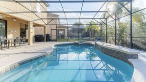 A swimming pool with a glass enclosure, outdoor seating area, and a covered patio. - Elsa's Enchanting Escape, just 15 minutes from Disney World! (Kissimmee)